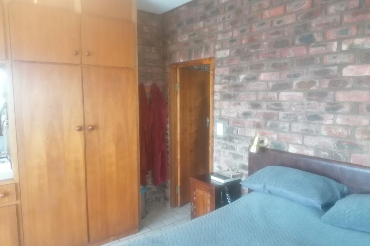 Bedroom featuring exposed brick wall, built-in wooden cabinetry, and tiled flooring.