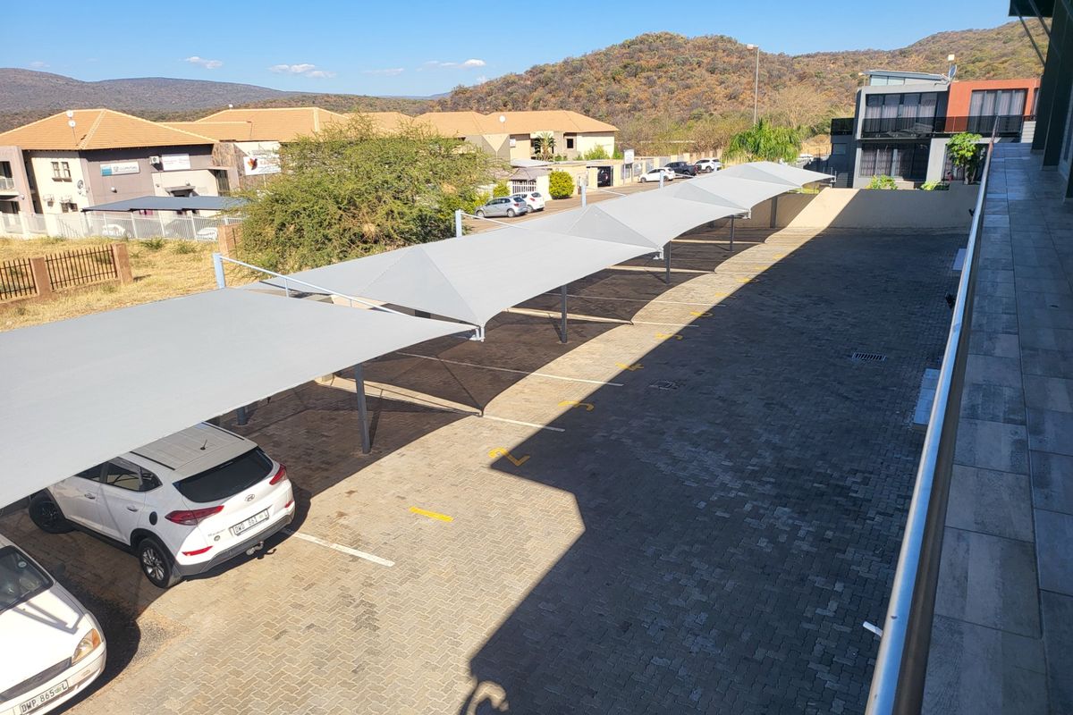 An elevated view of the apartment complex parking area featuring paved surfaces and covered shade-cloth parking bays.
