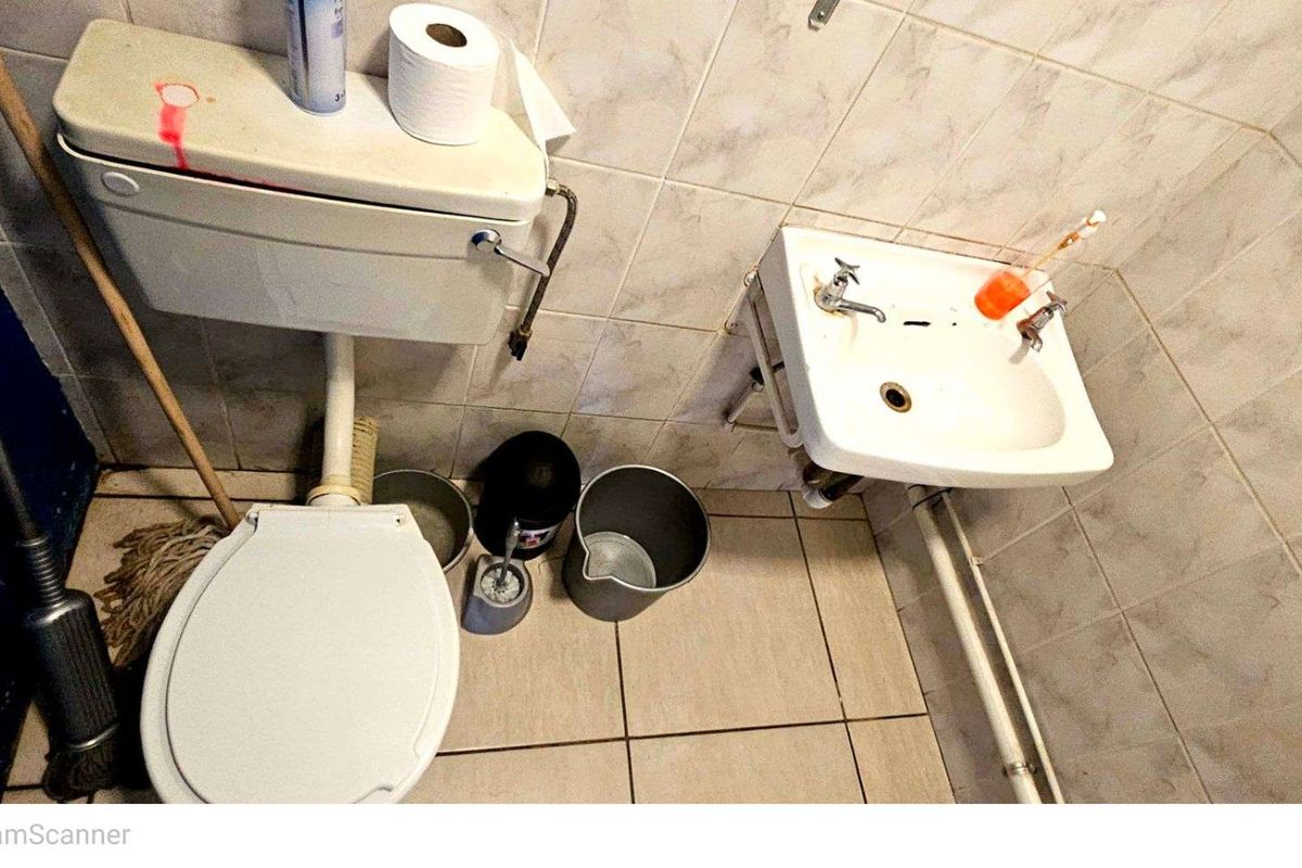 A compact bathroom featuring a wall-mounted basin and a standard toilet with tiled walls and flooring.
