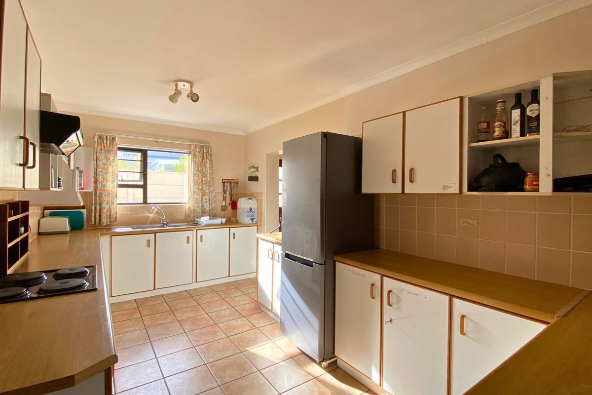 A functional kitchen featuring white cabinetry with wood trim, tiled flooring, a built-in hob, and an extractor fan.