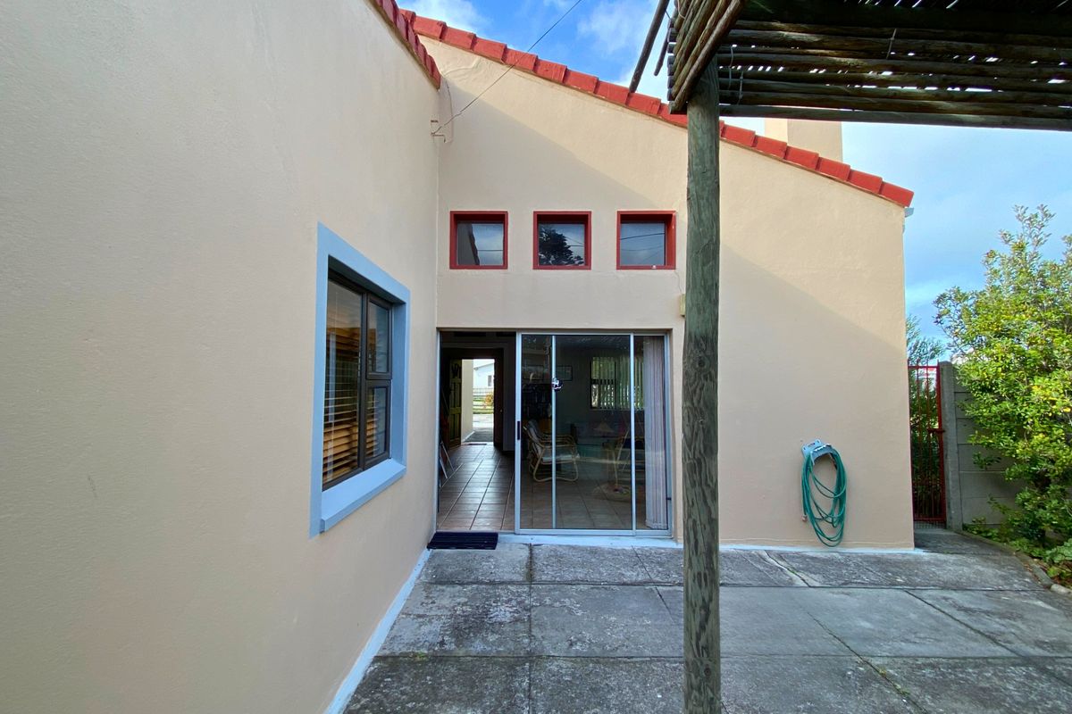 Rear exterior view featuring a paved patio area, sliding glass door access, and a timber pergola structure.