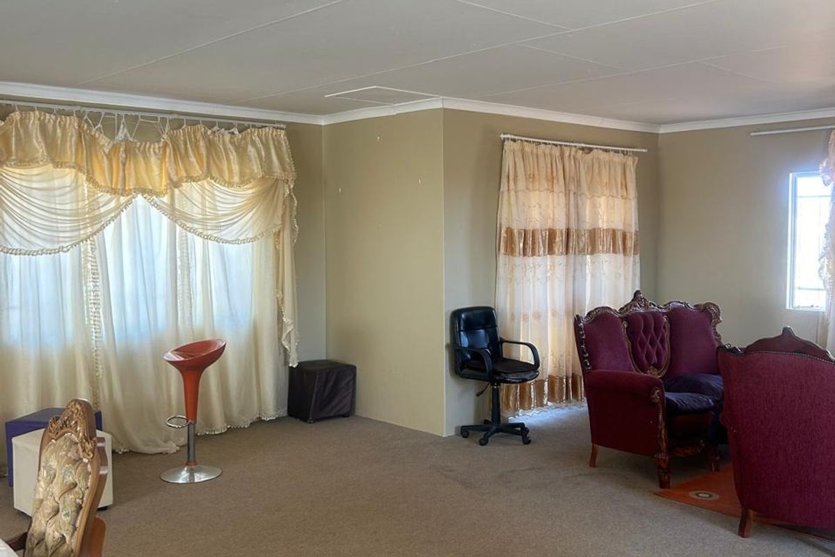 Spacious living area featuring neutral wall tones, carpeted flooring, and large windows with traditional drapery, offering a versatile layout for family living.