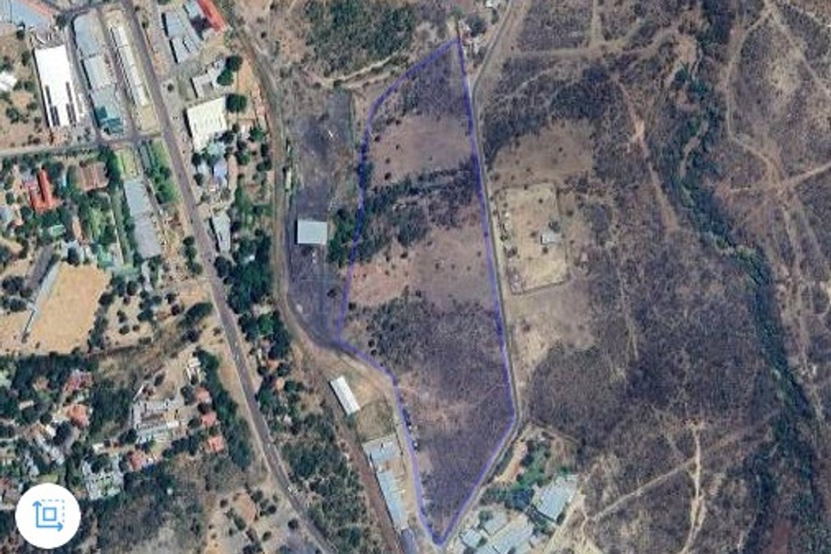 An aerial view of a large, undeveloped farm plot with a highlighted boundary, showing surrounding infrastructure and natural landscape.