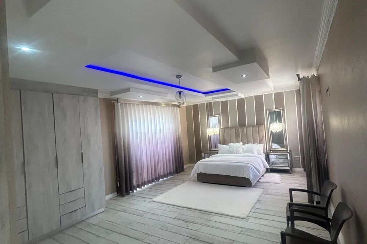 Spacious bedroom featuring a modern tray ceiling with integrated LED lighting, built-in wardrobes, and wood-look tiled flooring.