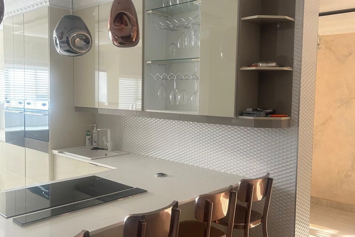 Modern kitchen featuring high-gloss cabinetry, integrated induction cooktop, stone countertops, and a breakfast bar with decorative pendant lighting.