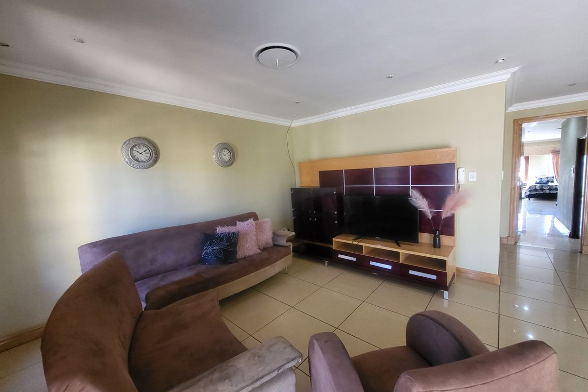 A spacious living room featuring large format floor tiles, crown molding, and a built-in media unit, with an open transition to the adjacent bedroom area.