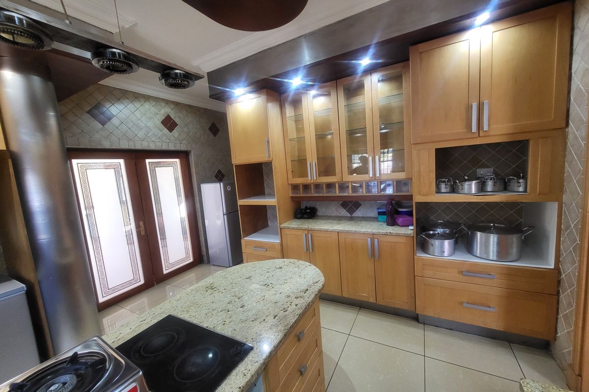 Spacious kitchen featuring light wood cabinetry, granite countertops, a central island with a built-in hob, and direct access to the patio through double doors.