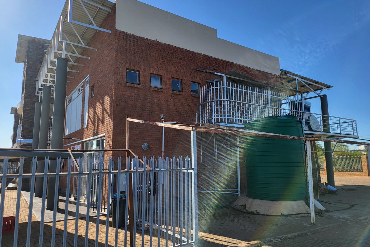 Exterior view of a commercial building featuring red brick facade, metal security fencing, and a large water storage tank.