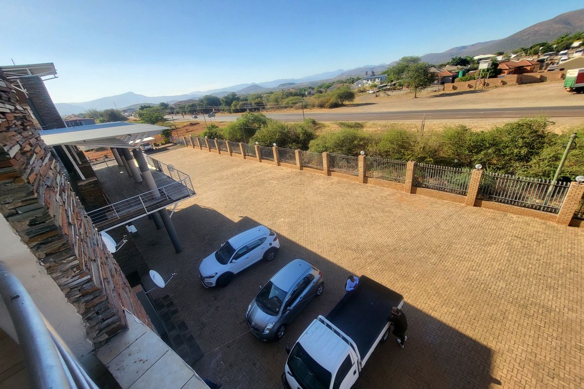 Elevated view of a paved commercial parking area and driveway, featuring stone-clad building exterior and perimeter fencing with mountain views in the background.