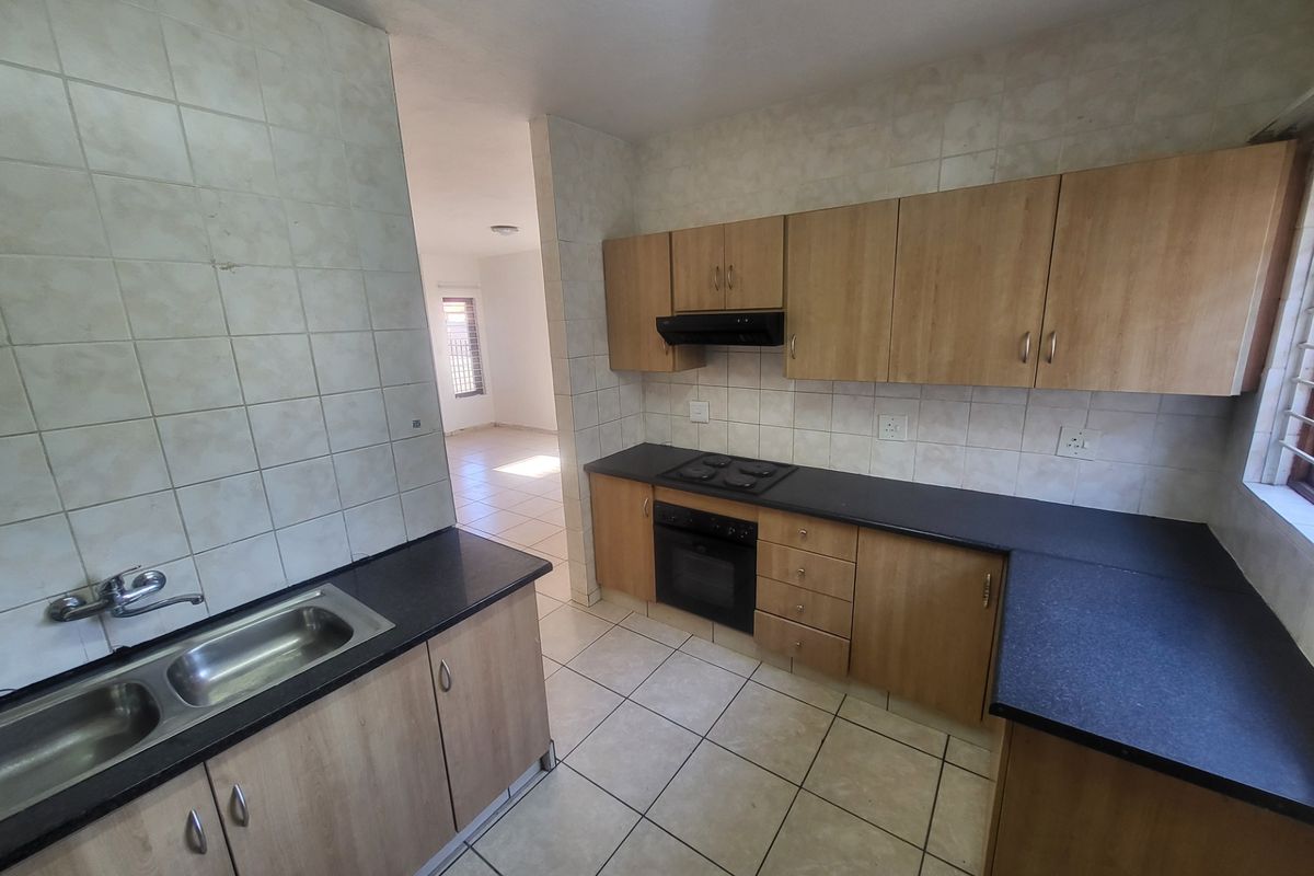Functional kitchen featuring light wood cabinetry, dark laminate countertops, built-in oven, hob, extractor fan, and double stainless steel sink with tiled splashbacks.