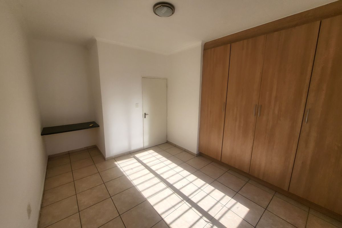 A bright, empty bedroom featuring tiled flooring, built-in wooden cabinetry, and a small wall-mounted desk area.