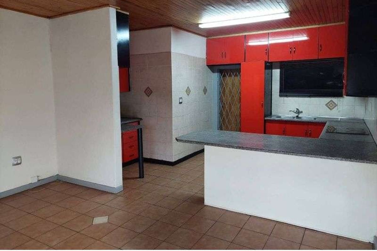 A dated kitchen featuring red cabinetry, a breakfast bar, tiled flooring, and a timber-paneled ceiling.