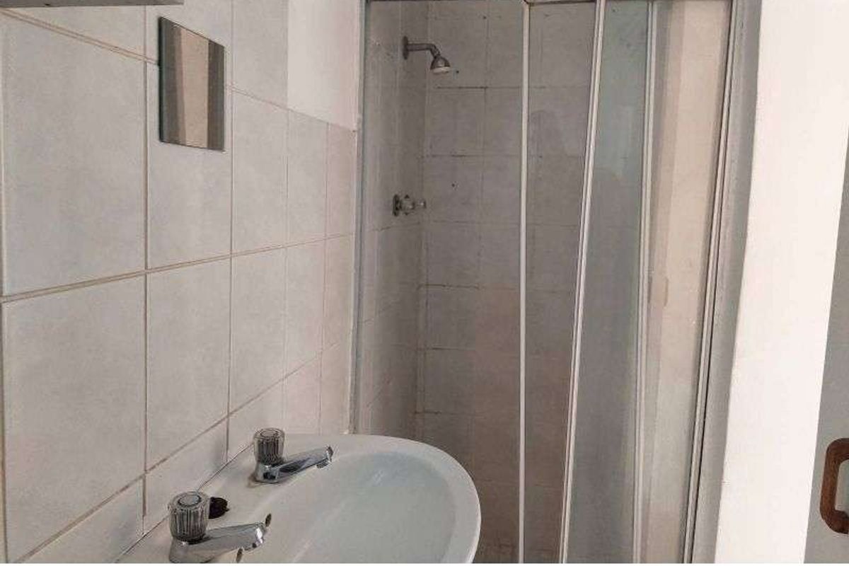 A functional bathroom featuring a shower enclosure with sliding glass doors and a wall-mounted basin with dual taps.
