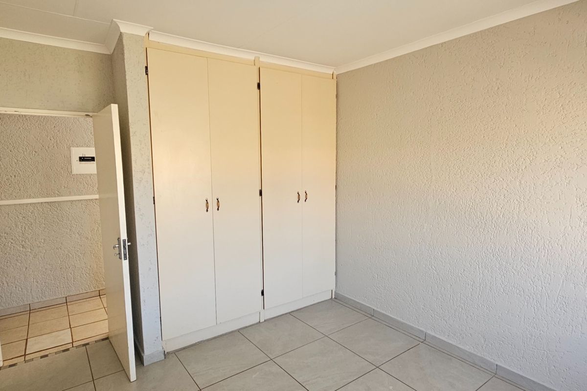 A bedroom featuring built-in cupboards, tiled flooring, and textured wall finishes, with an open doorway leading to an adjacent tiled area.
