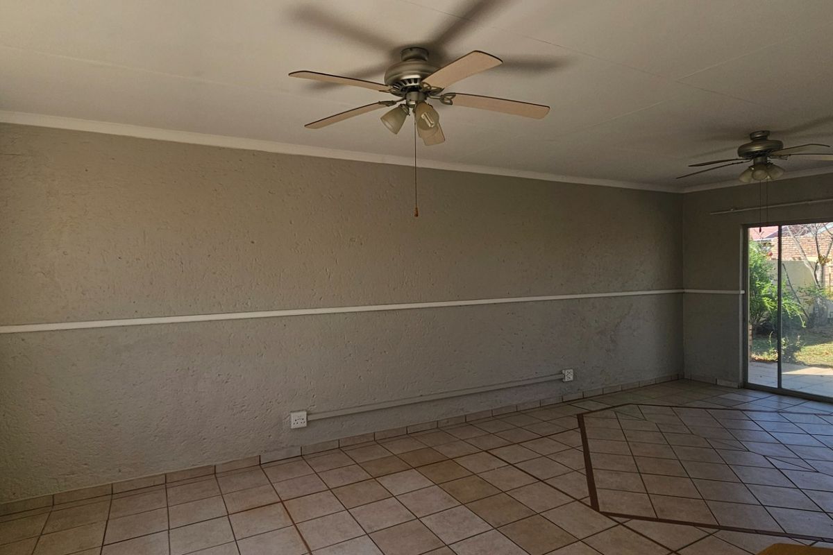 Spacious living area featuring tiled flooring, dual ceiling fans, and large sliding glass doors providing direct access to the rear garden.