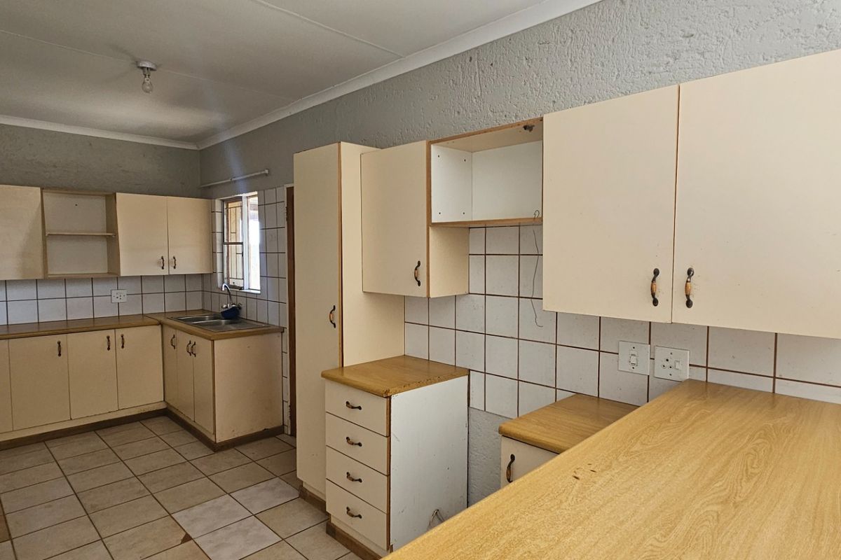 A dated kitchen featuring laminate cabinetry, tiled splashbacks, and tiled flooring, offering a functional layout in need of cosmetic updates.