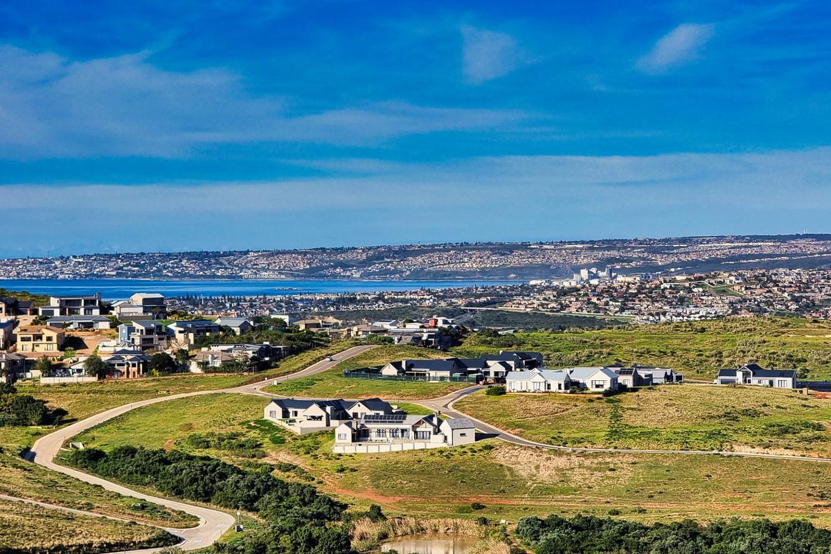 An elevated aerial view of a residential estate featuring rolling green hills, paved access roads, and distant coastal views.