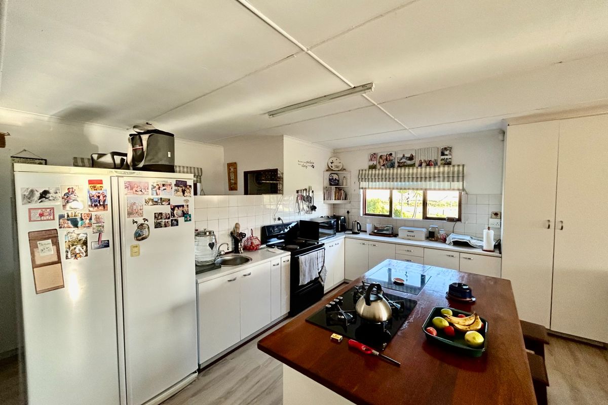 A functional kitchen featuring white cabinetry, a central wooden island with a built-in hob, and tiled splashbacks in a farm-style setting.
