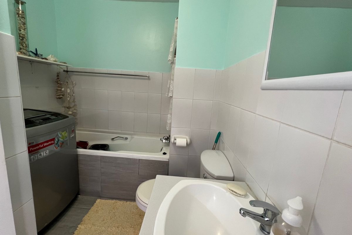 A functional bathroom featuring a built-in bathtub, vanity sink, and toilet, with tiled walls and space for a laundry appliance.