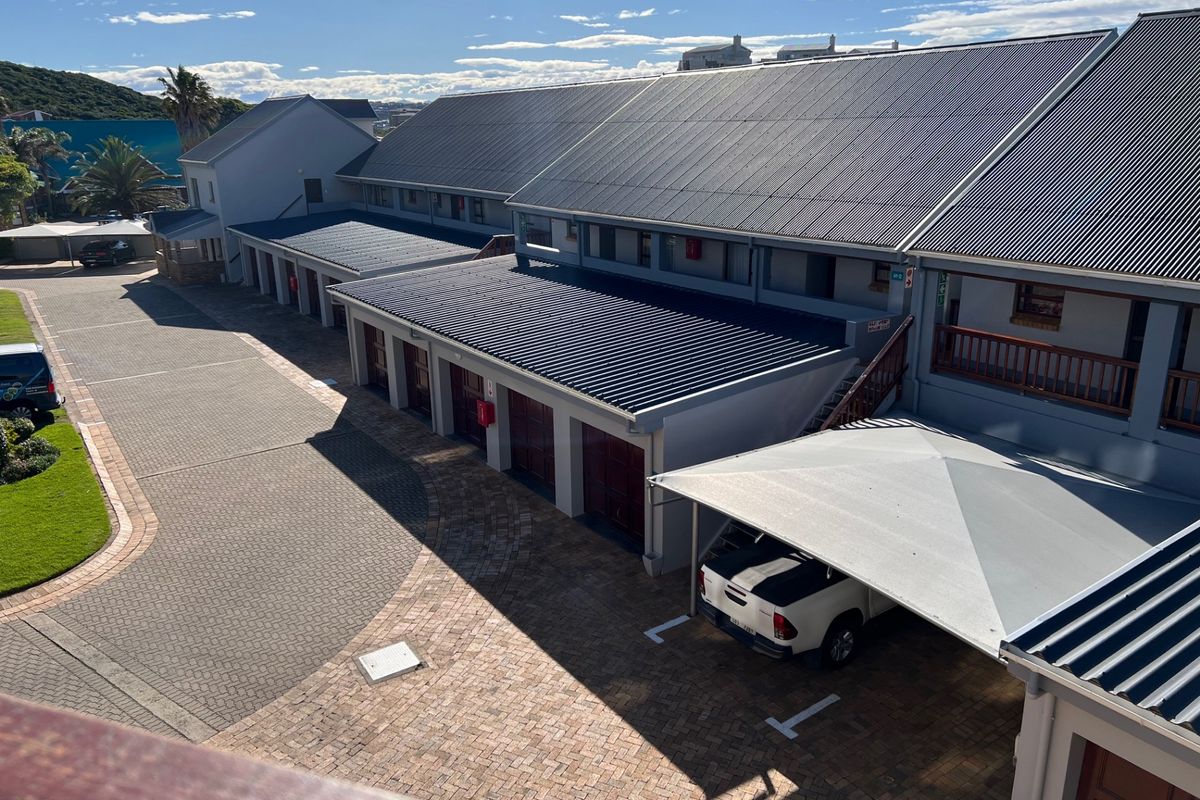 An elevated view of the apartment complex exterior, featuring paved parking areas, covered carports, and multiple garage units with metal roofing.
