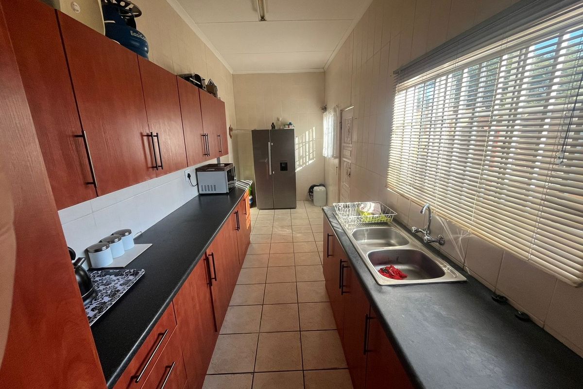 A functional galley-style kitchen featuring wood-finish cabinetry, dark countertops, a double stainless steel sink, and tiled flooring.