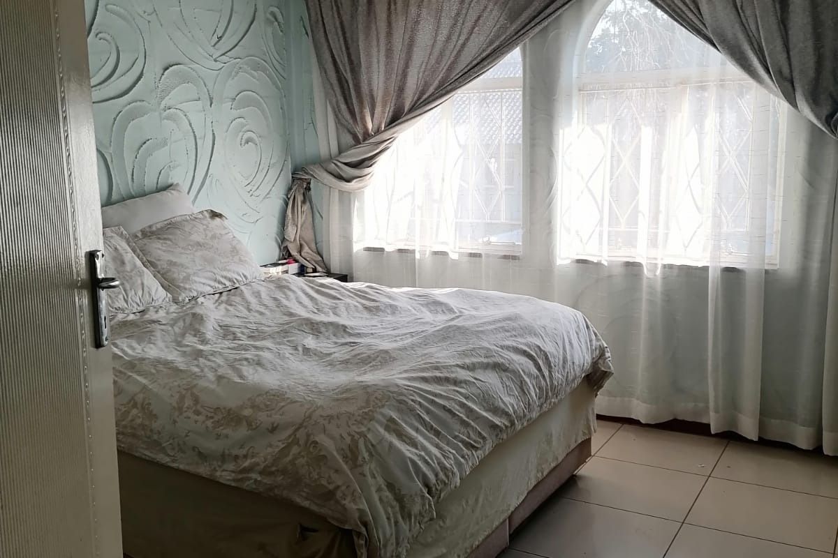 A bedroom featuring textured accent walls, tiled flooring, and arched windows with curtains, requiring cosmetic updates to modernize the space.