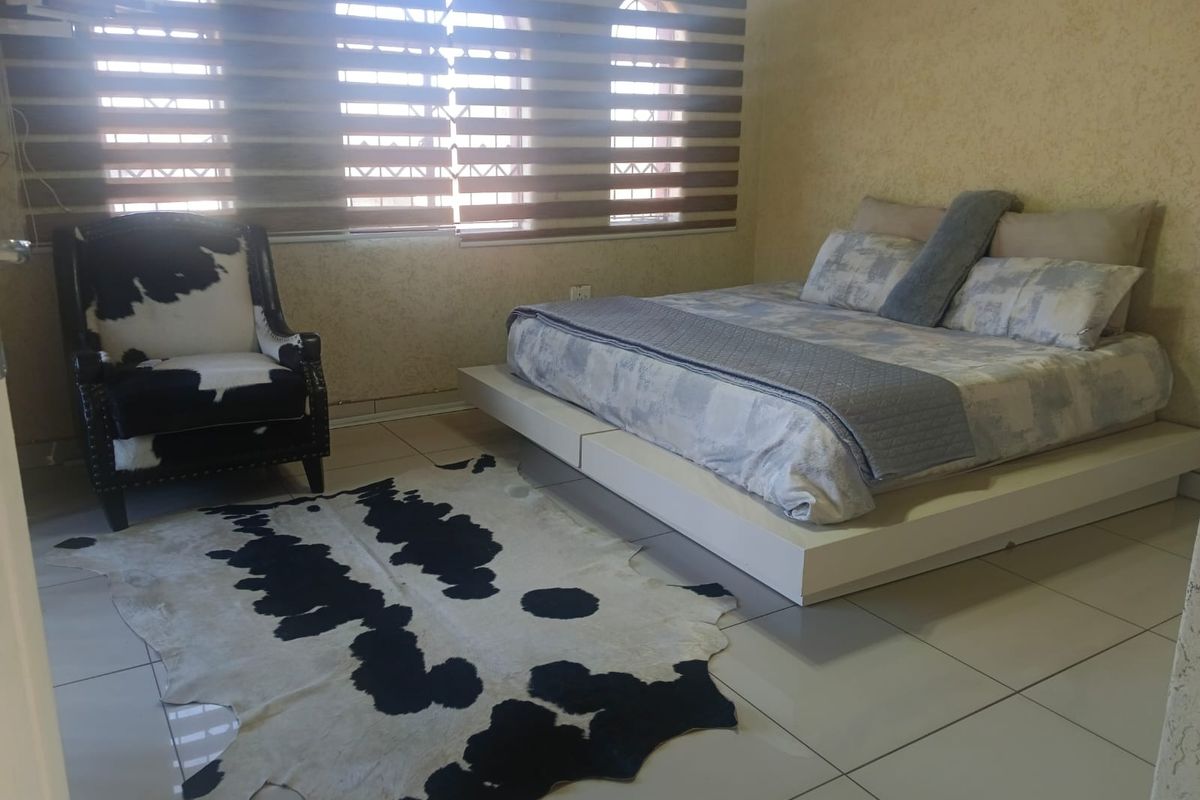 A spacious bedroom featuring tiled flooring, textured wall finishes, and arched windows fitted with modern zebra blinds.