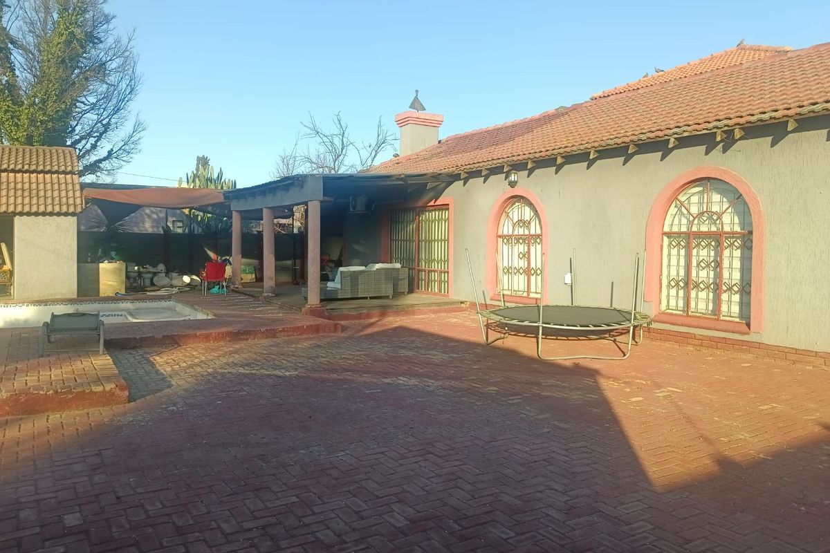 Rear exterior view featuring a paved patio area, swimming pool, and covered veranda with arched window detailing.