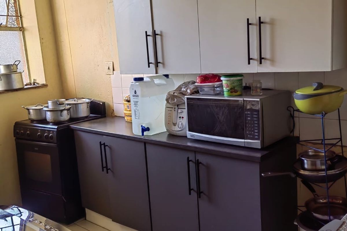 A functional kitchen featuring dark lower cabinetry, white upper cabinets, tiled flooring, and a freestanding stove.