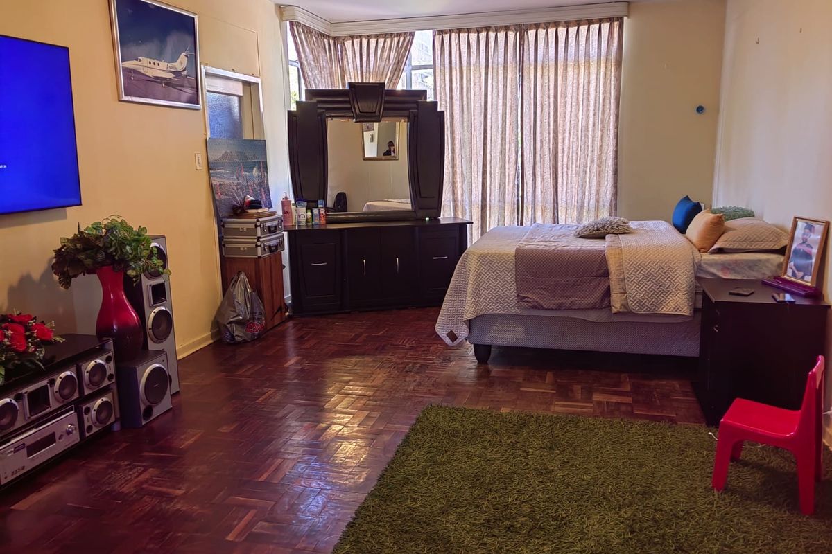 Spacious bedroom featuring classic parquet flooring, large windows with curtains, and ample room for a bed and storage furniture.