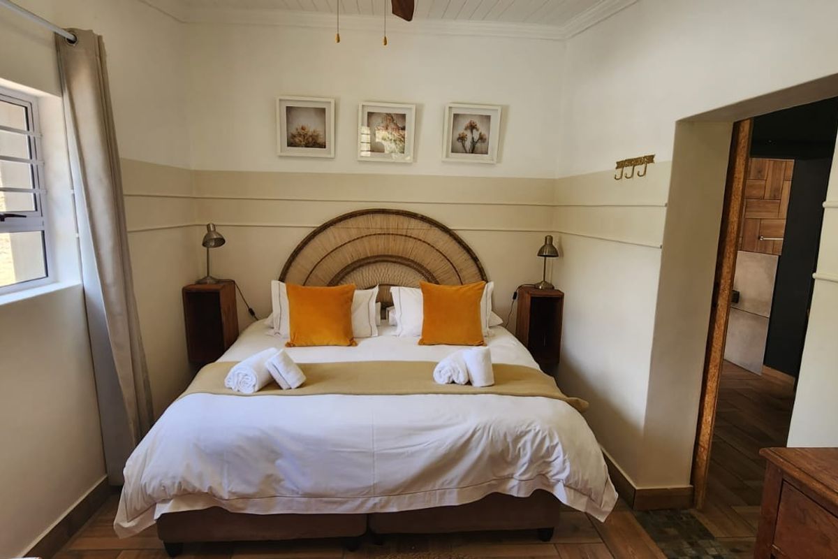 A well-maintained bedroom featuring neutral wall paneling, tiled flooring, and a window with natural light, leading into an adjacent bathroom area.