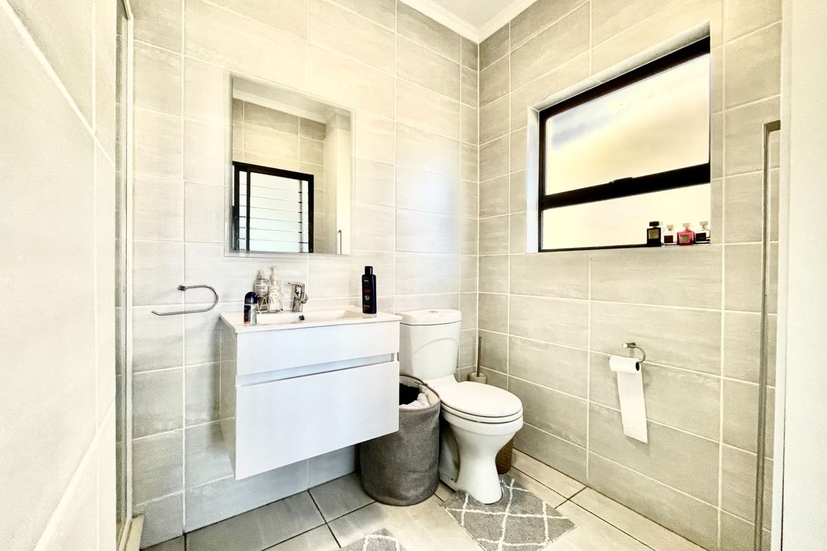 Modern bathroom featuring floor-to-ceiling neutral tiling, a wall-mounted vanity with integrated basin, and a toilet.