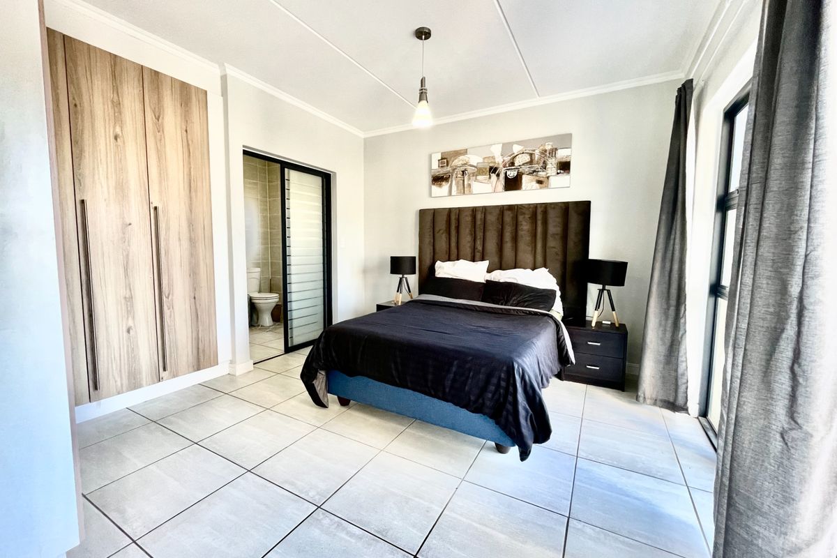 A well-maintained bedroom featuring large format floor tiles, built-in wooden cabinetry, and an en-suite bathroom with a sliding door entrance.