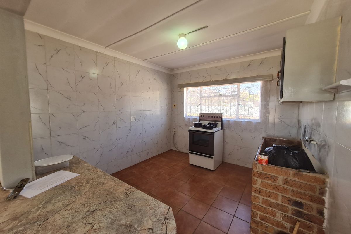 A functional kitchen space featuring tiled walls, a freestanding stove, and a brick-built counter base, offering potential for renovation and modernization.