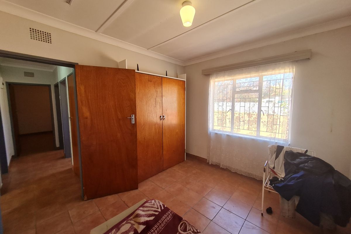 A bedroom featuring built-in wooden cupboards, tiled flooring, and a window with security bars, providing a functional and well-lit living space.
