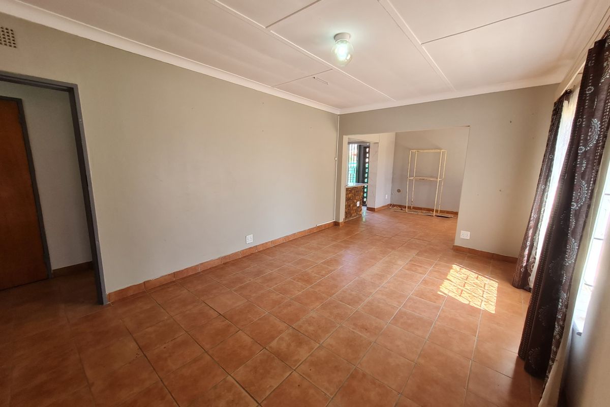 Spacious living area featuring neutral wall tones, tiled flooring, and a seamless transition into an adjacent room.
