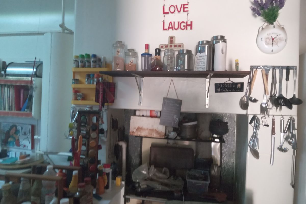 A kitchen area featuring wall-mounted shelving and utensil racks, showing signs of heavy use and dated finishes.