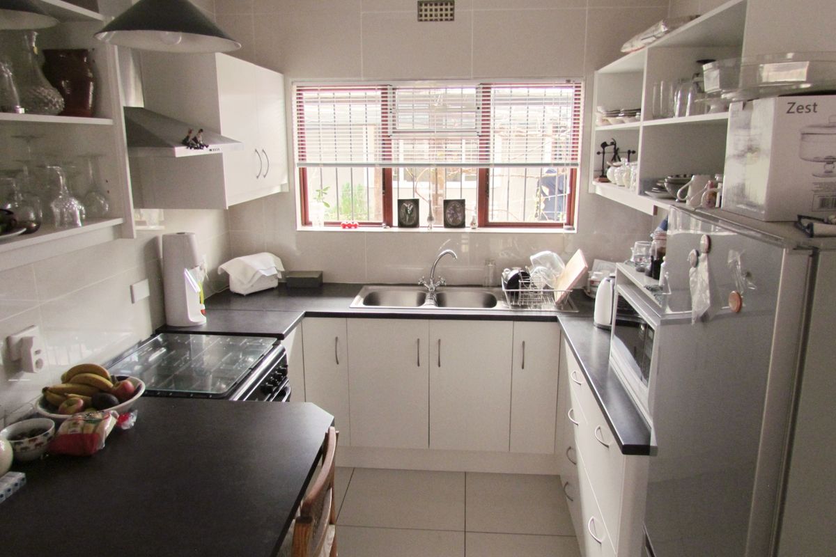 A functional kitchen featuring white cabinetry, dark countertops, a double-basin sink, and built-in extractor fan, offering a clean and practical workspace.