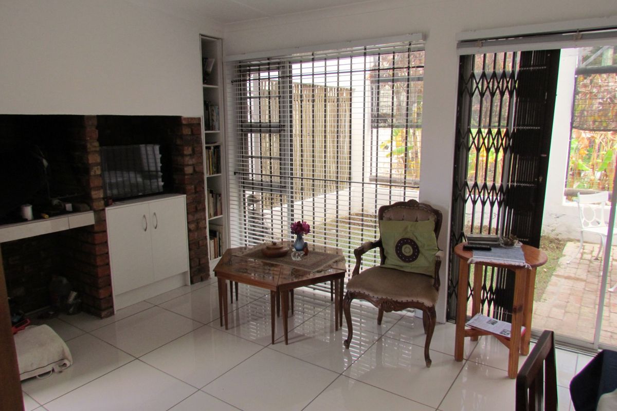 A living room featuring tiled flooring, a built-in brick fireplace, integrated shelving, and large windows with blinds leading to an outdoor area.
