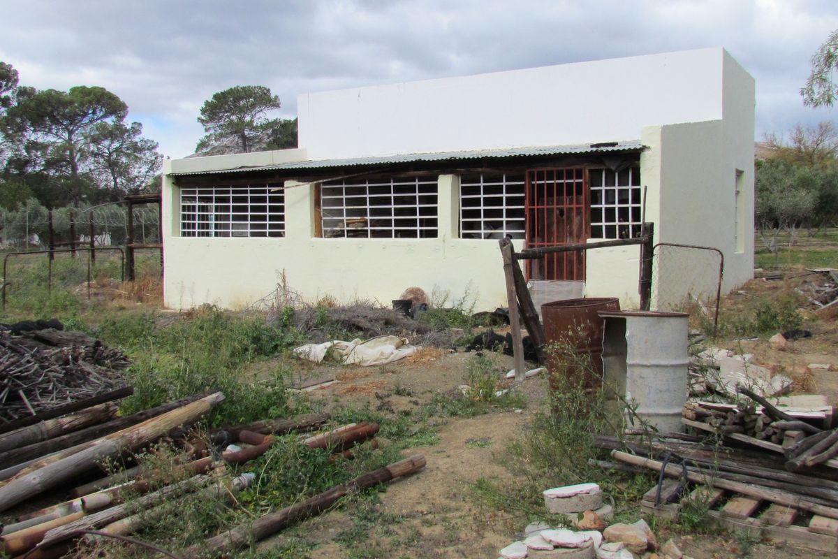 A detached structure in need of significant renovation, featuring a simple facade with security bars and a corrugated metal roof.