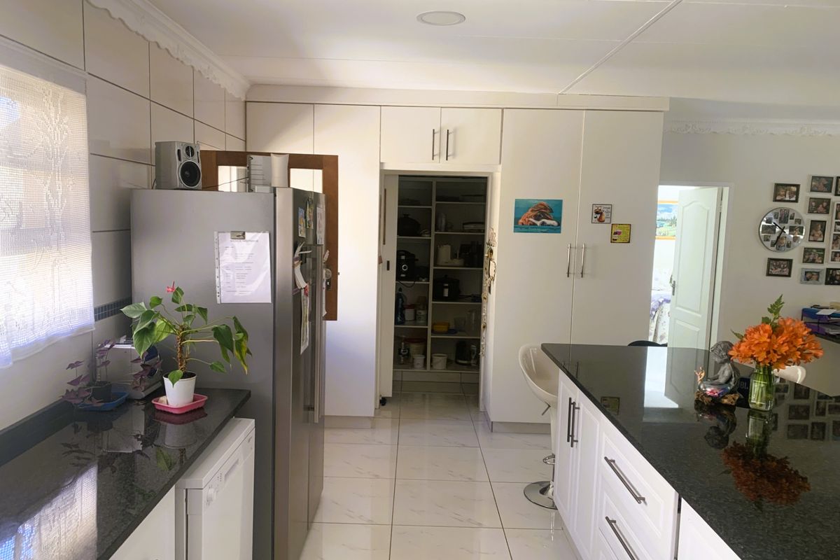 A bright kitchen featuring white cabinetry, dark granite countertops, a central island, and a convenient walk-in pantry area.