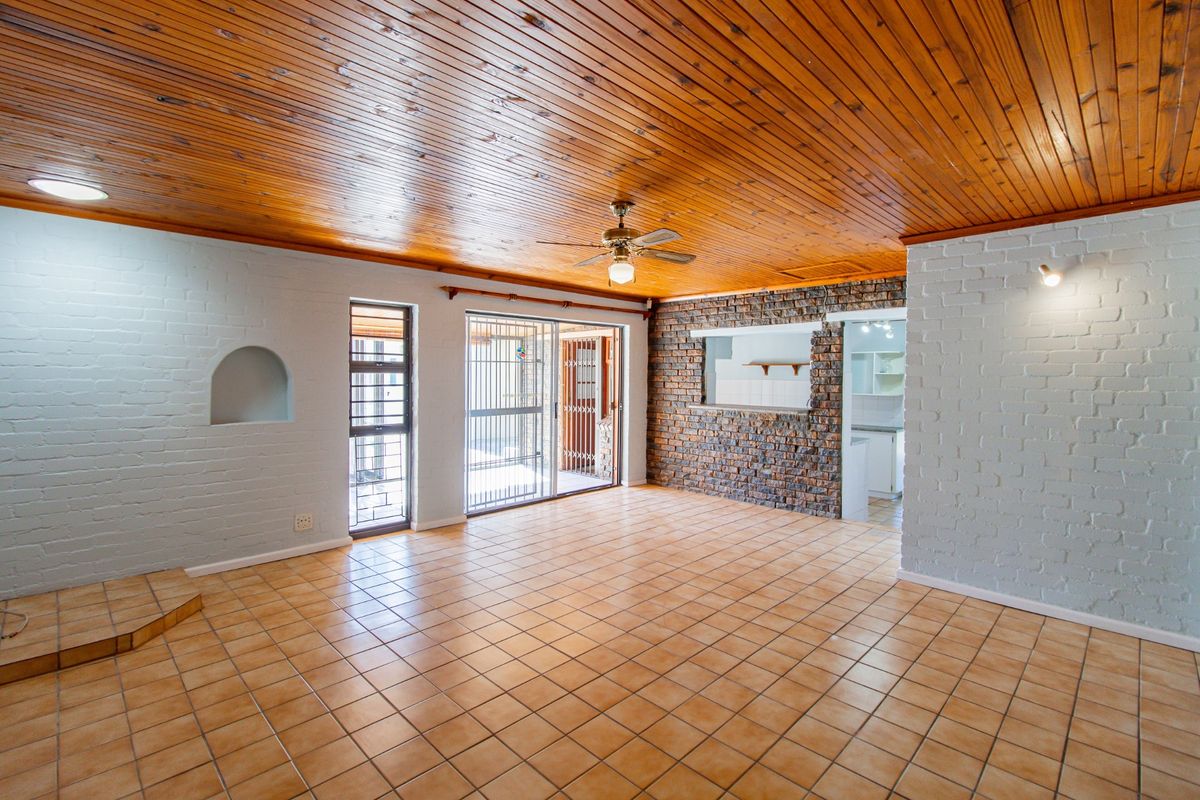 Spacious living area featuring a timber-clad ceiling, tiled flooring, exposed brick feature wall, and sliding door access to the outdoor patio.