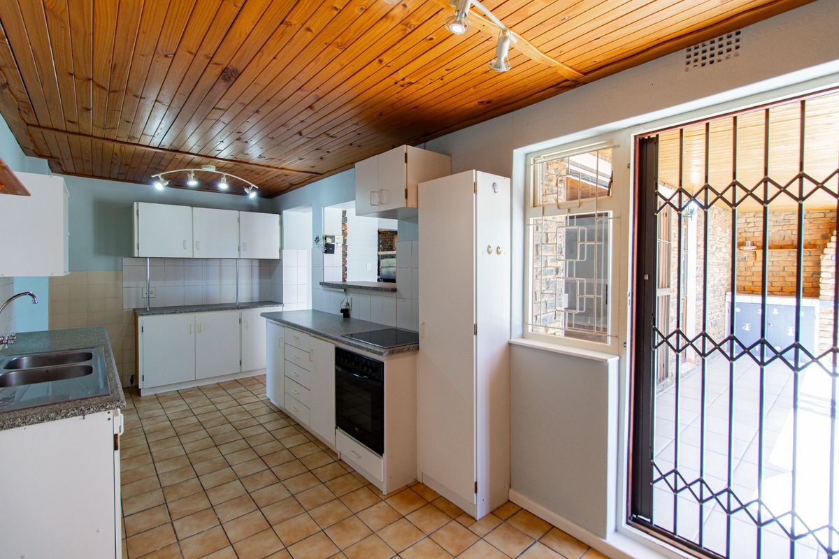 Functional kitchen featuring white cabinetry, built-in oven and hob, tiled flooring, and a timber-clad ceiling with direct access to the outdoor patio area.