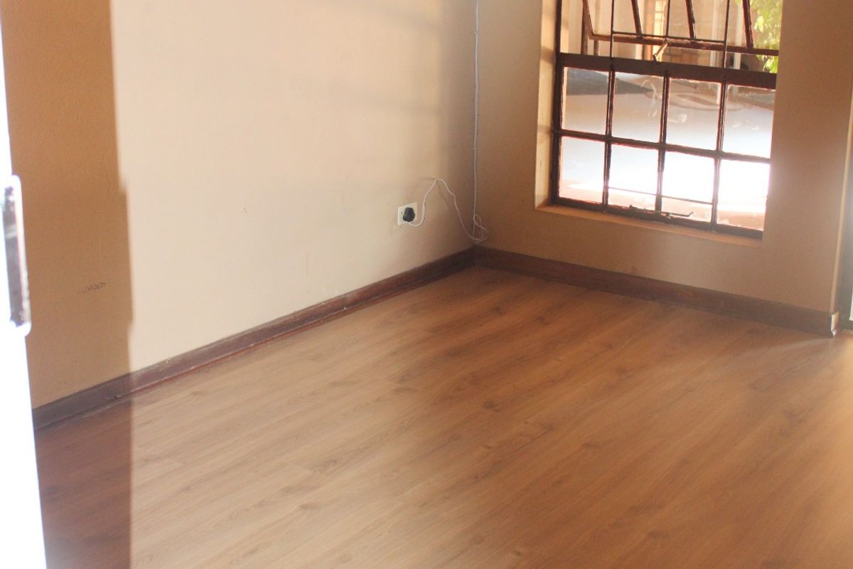 An empty bedroom featuring light wood-look laminate flooring, a large multi-pane window, and wall-mounted lighting.
