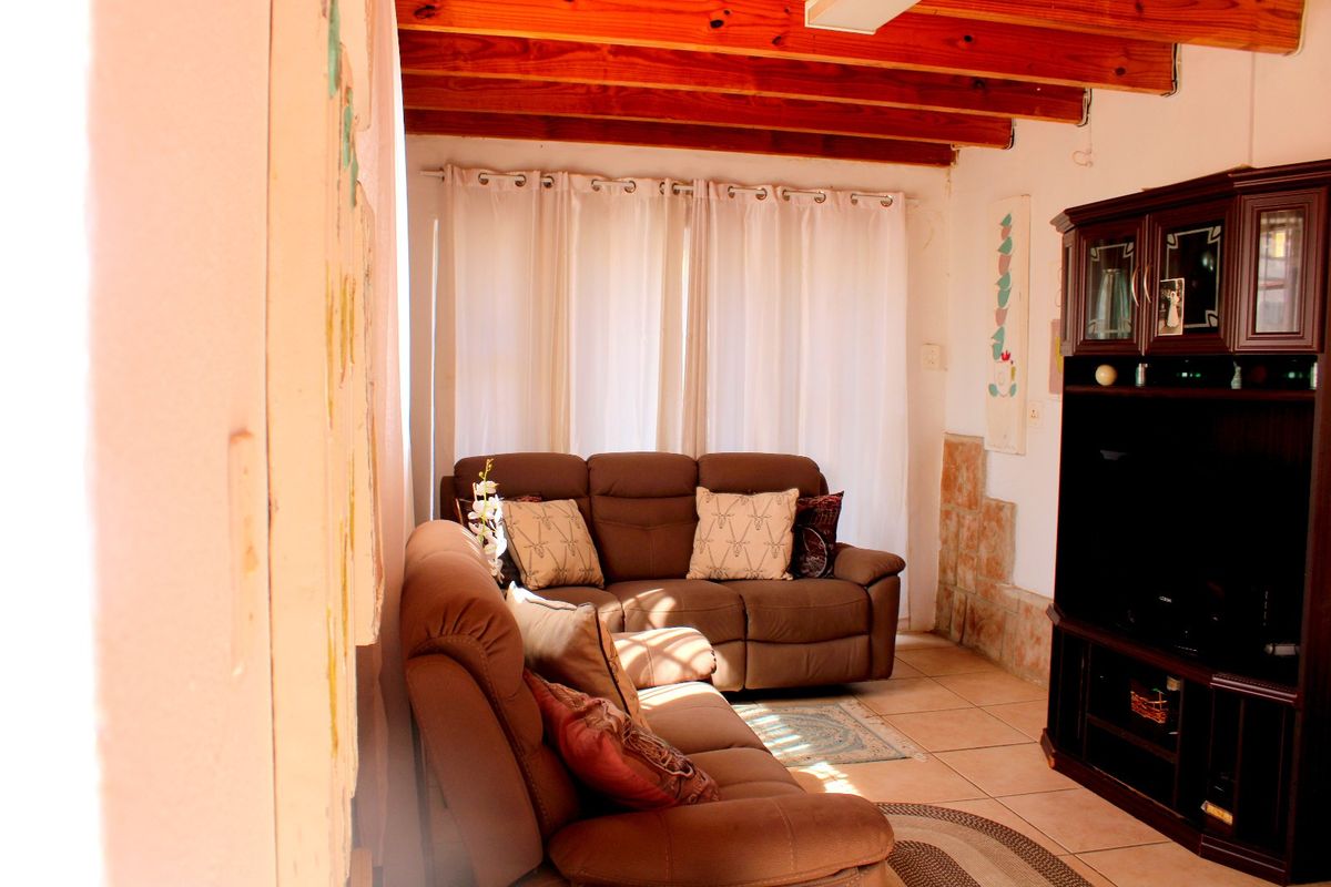 A cozy living room featuring exposed timber ceiling beams, tiled flooring, and large windows with natural light.