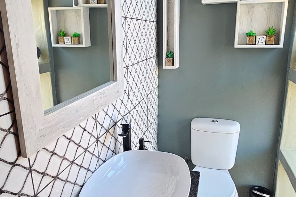 A compact bathroom featuring a modern vessel sink on a vanity, a toilet, and decorative wall shelving against a patterned accent wall.