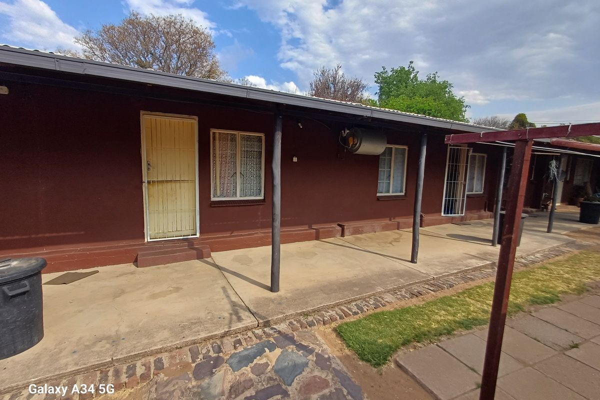 Rear exterior view of the house featuring a covered concrete patio, security gates, and an external geyser unit.