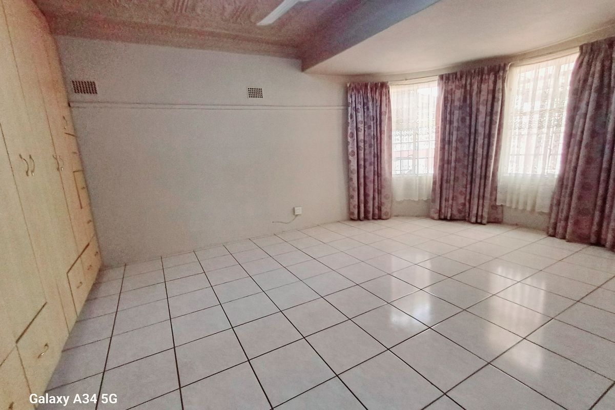 A spacious bedroom featuring tiled flooring, built-in cabinetry, and a ceiling fan, offering a clean and functional living space.