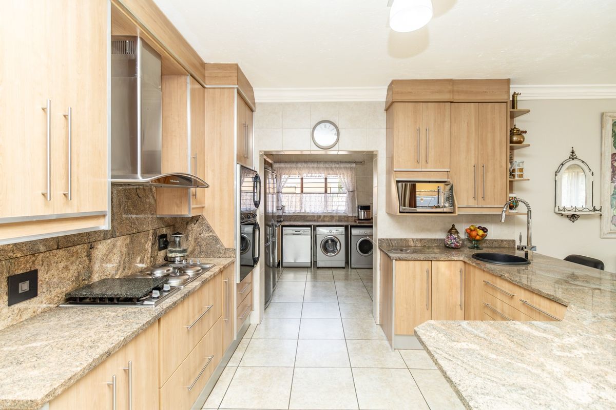 A well-appointed kitchen featuring light wood cabinetry, granite countertops, a gas hob, extractor fan, and an integrated oven, with an adjoining scullery area.