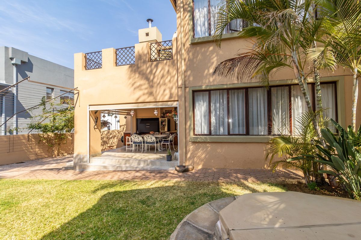 Rear view of the property featuring a covered patio area, landscaped garden, and a balcony with a built-in chimney stack.